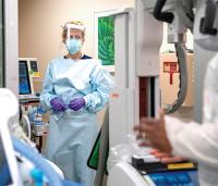 A healthcare worker in full protective gear stands in a hospital room.